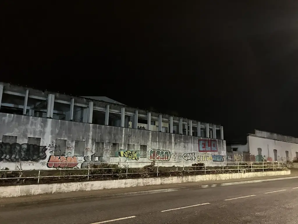Antigua fábrica en Póvoa de Varzim, Portugal, fotografiada de noche. Sus paredes están cubiertas de grafitis y se percibe un ambiente urbano y decadente bajo el cielo oscuro.