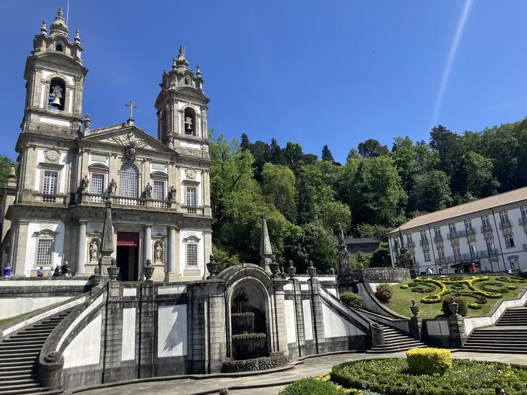 Fachada principal del Santuario del Bom Jesus do Monte con sus dos torres y una fuente decorativa al frente, rodeada de jardines geométricos.