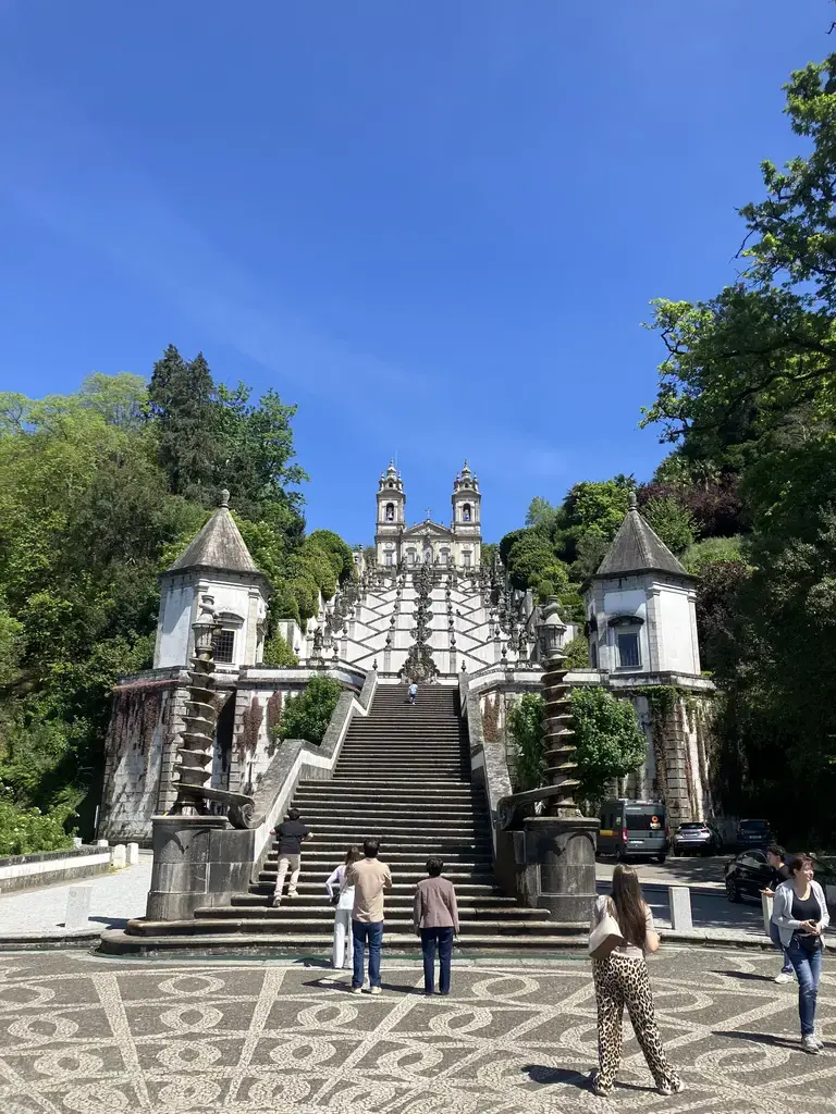 Vista frontal del Santuario del Bom Jesus do Monte en Braga, Portugal, con su emblemática escalera barroca y visitantes subiendo los escalones.