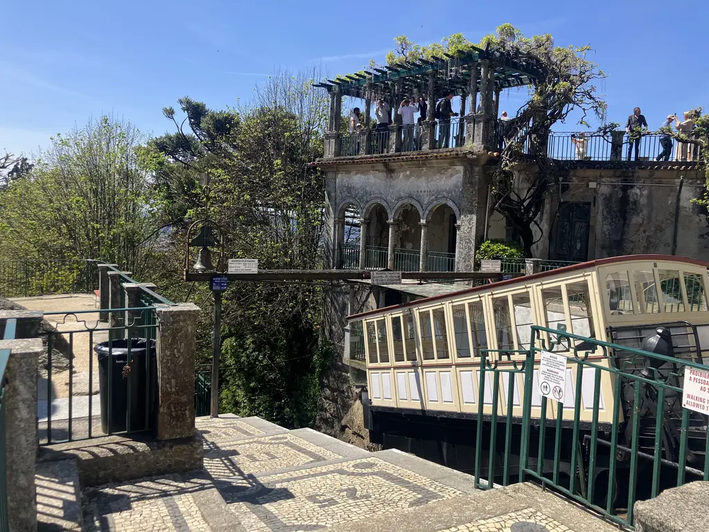 Plano del funicular de Bom Jesus do Monte junto a un edificio con terraza cubierta de vegetación y visitantes observando desde arriba.