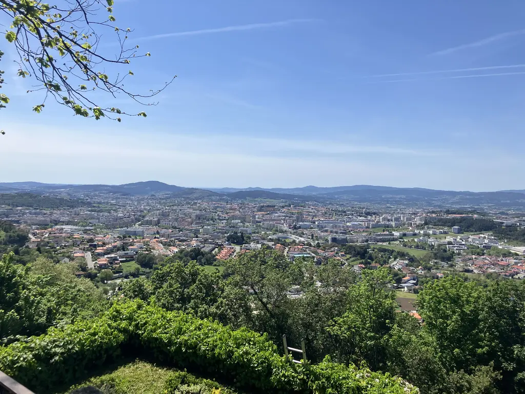 Vista amplia de Braga desde lo alto del santuario, con colinas al fondo y árboles enmarcando la imagen.