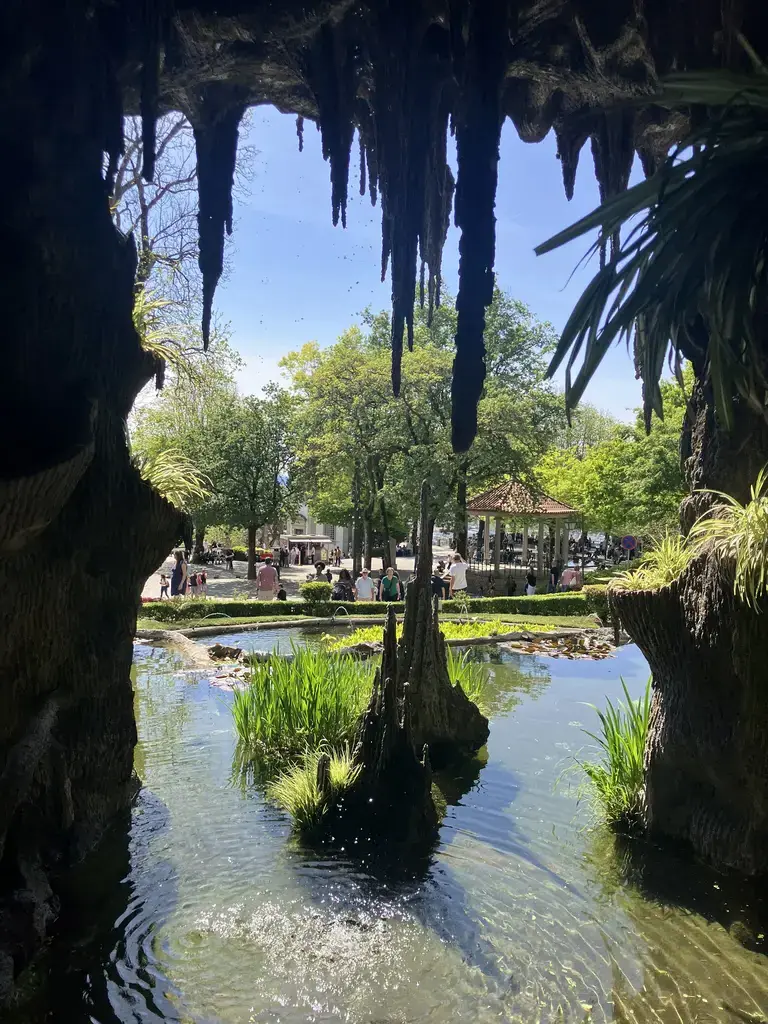 Vista desde el interior de la gruta, mostrando el estanque con plantas acuáticas y visitantes paseando al fondo.