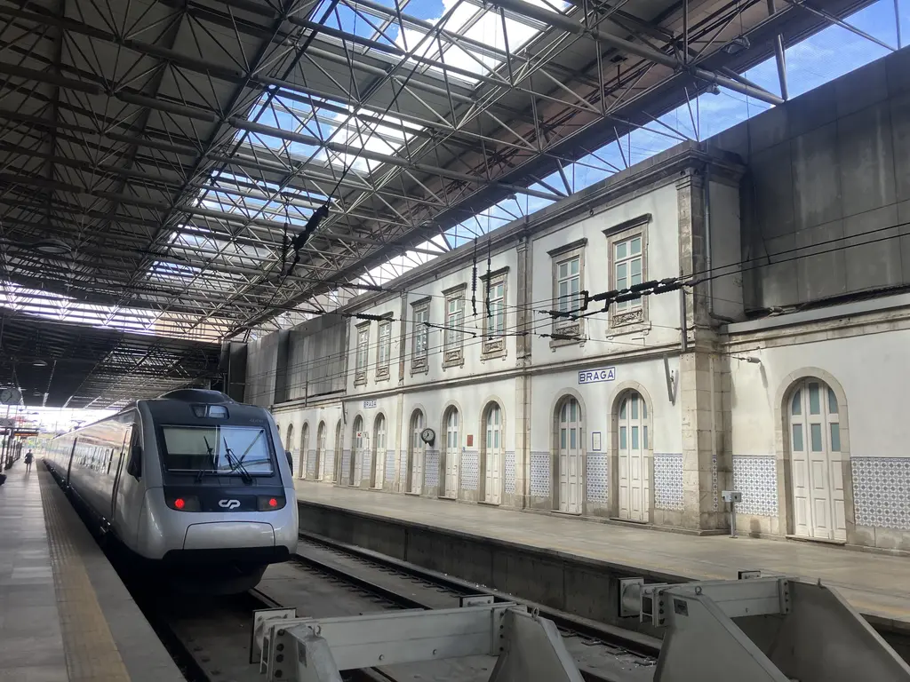 Andén de la estación de tren de Braga, con un tren moderno detenido junto al edificio blanco con azulejos típicos portugueses.